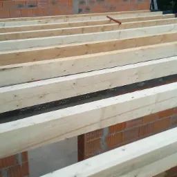 Montaż drewnianej konstrukcji dachu na murze z cegły, z izolacją przeciwwilgociową na belkach nośnych.