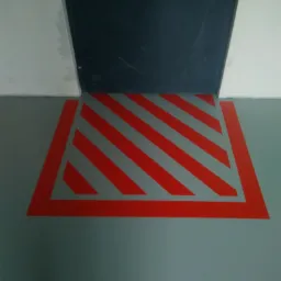 Szara posadzka żywiczna z czerwonymi, ukośnymi pasami ostrzegawczymi przy ciemnych drzwiach.