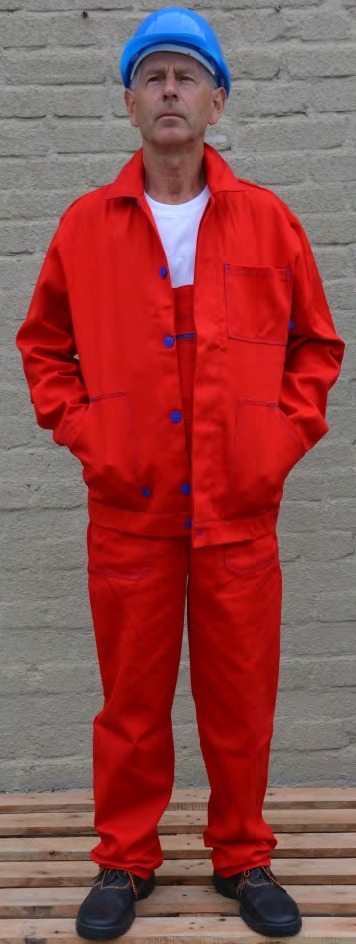 Mężczyzna w czerwonym kombinezonie roboczym z niebieskimi guzikami i niebieskim kasku ochronnym, stojący na tle ceglanej ściany.