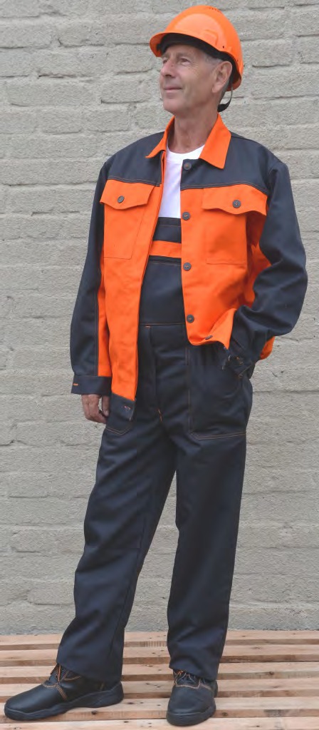 Mężczyzna w pomarańczowo-granatowym komplecie odzieży roboczej i pomarańczowym kasku ochronnym, stojący na drewnianej palecie na tle szarej ściany z cegły.