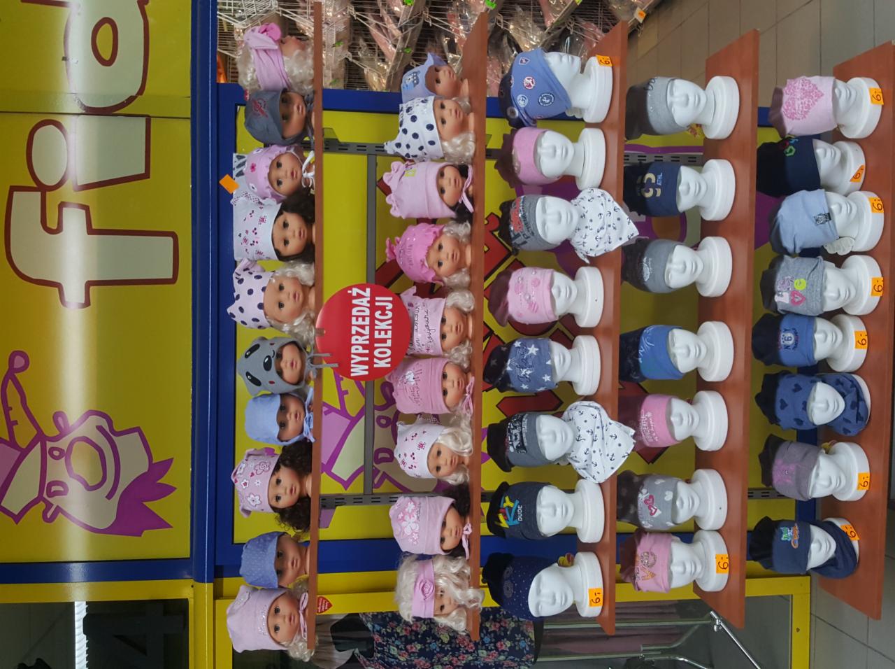 Wyprzedaż kolekcji czapek dziecięcych na manekinach głowach w sklepie, widoczne różne wzory i kolory czapek na półkach.