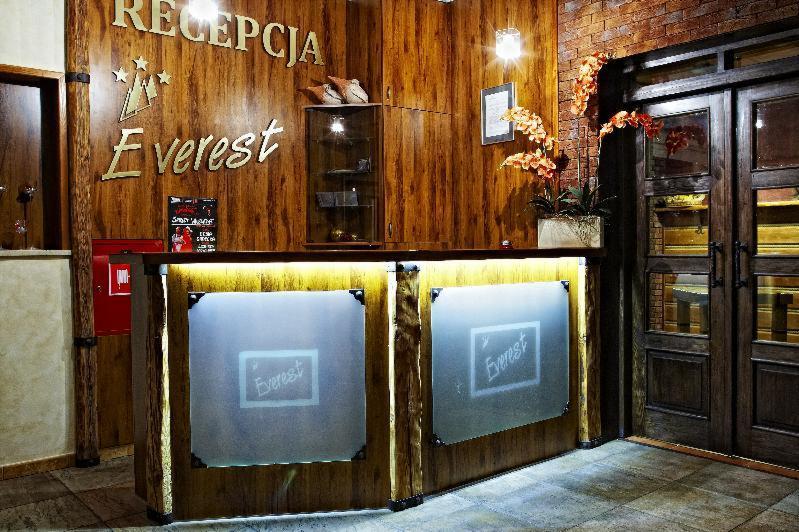 Recepcja hotelu Everest z drewnianą okładziną, podświetlanym blatem i logo na szklanych panelach, uzupełniona kwiatami i dekoracyjnymi elementami.
