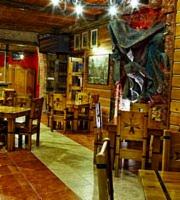 Rustykalne wnętrze restauracji z drewnianymi ścianami, krzesłami i stołami, oświetlone ciepłym światłem lamp.