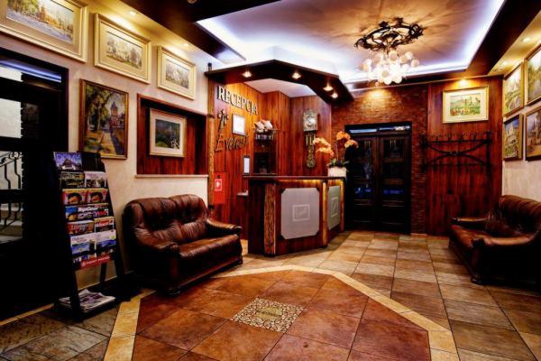 Rustykalne wnętrze hotelu z drewnianą recepcją, skórzaną sofą i dekoracyjnymi obrazami na ścianach, oświetlone ozdobnym żyrandolem.