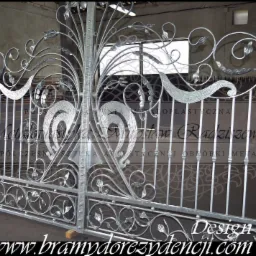 Surowa, srebrna brama z kutego metalu z motywami roślinnymi, model Design E-19, widoczna w warsztacie przed montażem.