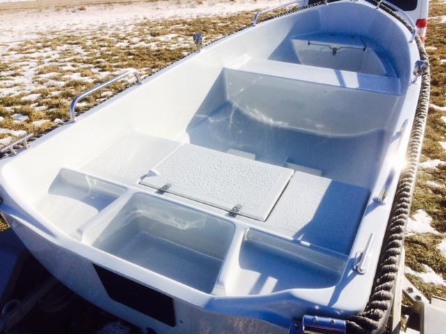 Biała łódka z tworzywa sztucznego, z widocznymi schowkami i liną cumowniczą, stojąca na trawie pokrytej śniegiem.