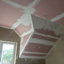 Skośny sufit poddasza z płyt kartonowo-gipsowych, częściowo wyszpachlowany, widoczne łączenia i przewód elektryczny.