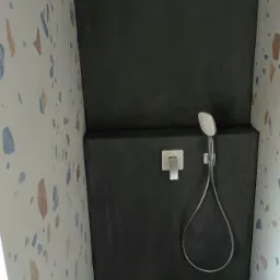 Kabina prysznicowa z czarnymi płytkami i armaturą w kolorze chromu, ściany wyłożone płytkami w stylu terrazzo z kolorowymi elementami.