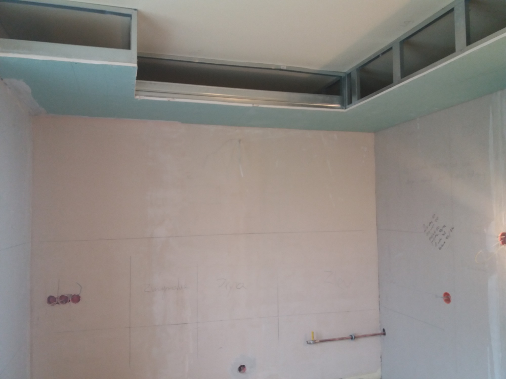 Wnętrze w trakcie remontu: ściany z płyt gipsowo-kartonowych z widocznymi liniami podziału i napisem ołówkiem, metalowa konstrukcja sufitu podwieszanego z płytą GK w kolorze zielonym, instalacja...