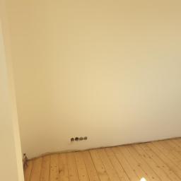 MatBud - Pomalowane na kremowo ściany i drewniana podłoga w pokoju w Ostrowie Wielkopolskim, widoczne gniazdka elektryczne przy podłodze.