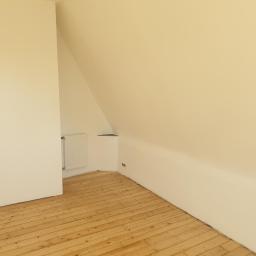 MatBud - Poddasze z drewnianą podłogą i pomalowanymi na kremowo ścianami, widoczny grzejnik i skośny sufit.