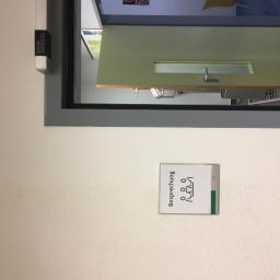 MatBud - Fragment ściany biura z tabliczką informacyjną 'Besprechung' (spotkanie) i widokiem na salę konferencyjną przez otwarte drzwi.