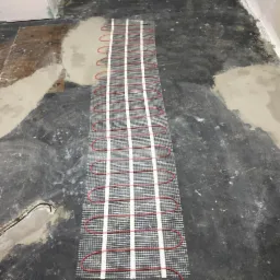 Montaż maty grzewczej pod wylewkę na nierównym, przygotowywanym podłożu w pomieszczeniu.