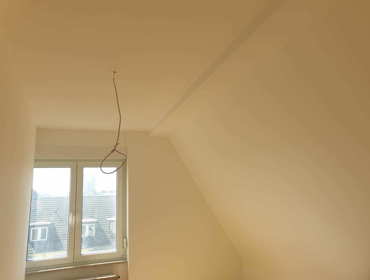 Świeżo pomalowane poddasze ze skosem, widoczne okno dachowe i wiszący przewód elektryczny