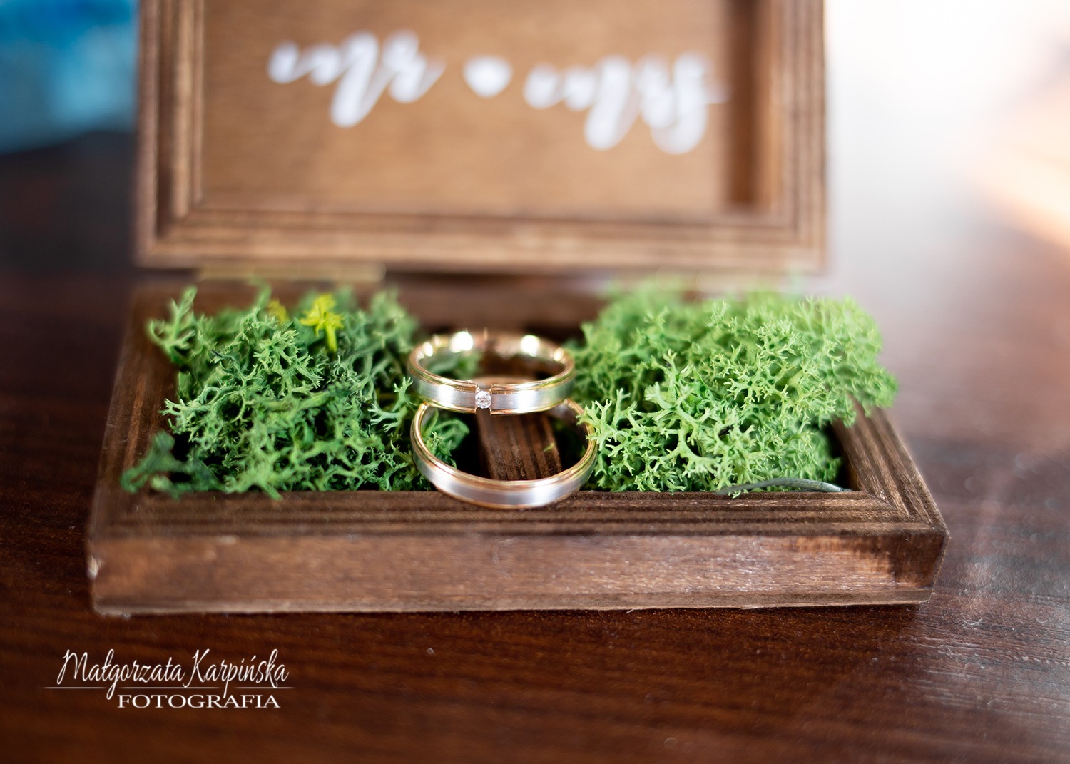 Obrączki ślubne w drewnianym pudełku wypełnionym mchem, z napisem 'Mr & Mrs' w tle.