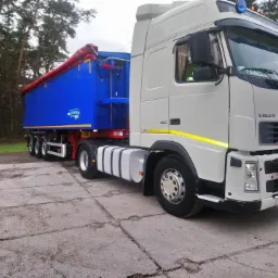 Biała ciężarówka Volvo z niebieską naczepą wywrotką na betonowym placu, widoczne tablice rejestracyjne i napis 'PAWEL' na szybie.