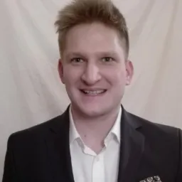 Uśmiechnięty mężczyzna w garniturze i białej koszuli, z poszetką w kieszonce, na jasnym tle. Portret biznesowy.