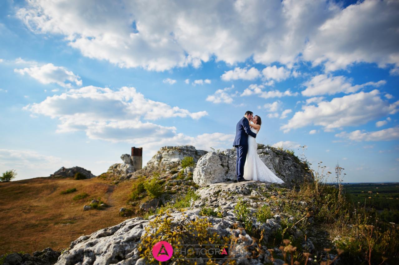Para młoda całująca się na szczycie wapiennej skały z ruinami zamku w tle, błękitne niebo z obłokami.