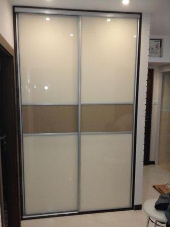 Dwudrzwiowa szafa przesuwna z kremowymi i brązowymi panelami, obramowana ciemnym drewnem, w jasnym wnętrzu.