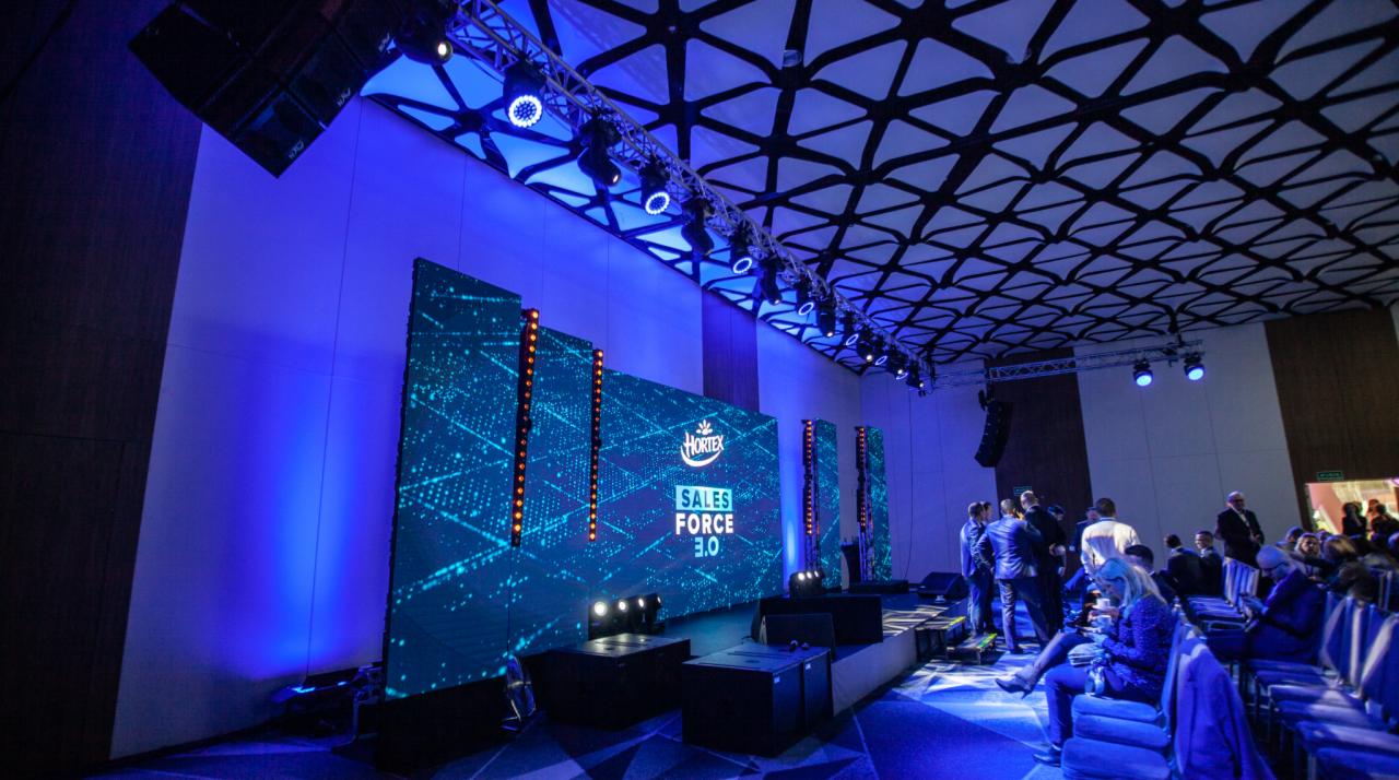 Konferencja z podświetloną sceną i ekranem LED z logo Hortex Sales Force 3.0, oświetlenie sceniczne w odcieniach niebieskiego, widoczni uczestnicy w tle.
