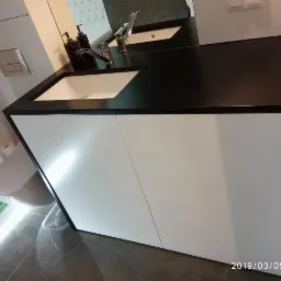 Nowoczesna łazienka z białą szafką pod umywalkę z czarnym blatem, widoczna toaleta podwieszana i marmurowe płytki podłogowe.