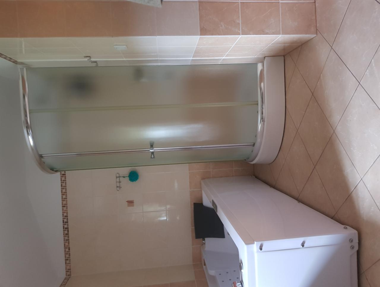 Nowoczesna kabina prysznicowa z matowym szkłem i chromowanymi elementami, umieszczona w narożniku łazienki wyłożonej beżowymi płytkami, obok widoczna wanna z hydromasażem i czarnym panelem sterowania.