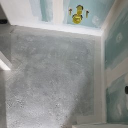 Usługi Budowlane Łukasz Jaromieńczuk - Łazienka w trakcie remontu: ściany po szpachlowaniu, sufit z zielonymi płytami gipsowo-kartonowymi i żółtymi rurami instalacji hydraulicznej.