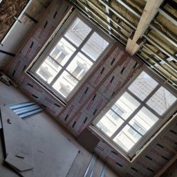 Usługi Budowlane Łukasz Jaromieńczuk - Montaż izolacji termicznej wokół okien dachowych w trakcie poddasza, widoczne profile metalowe konstrukcji sufitu i wełna mineralna.