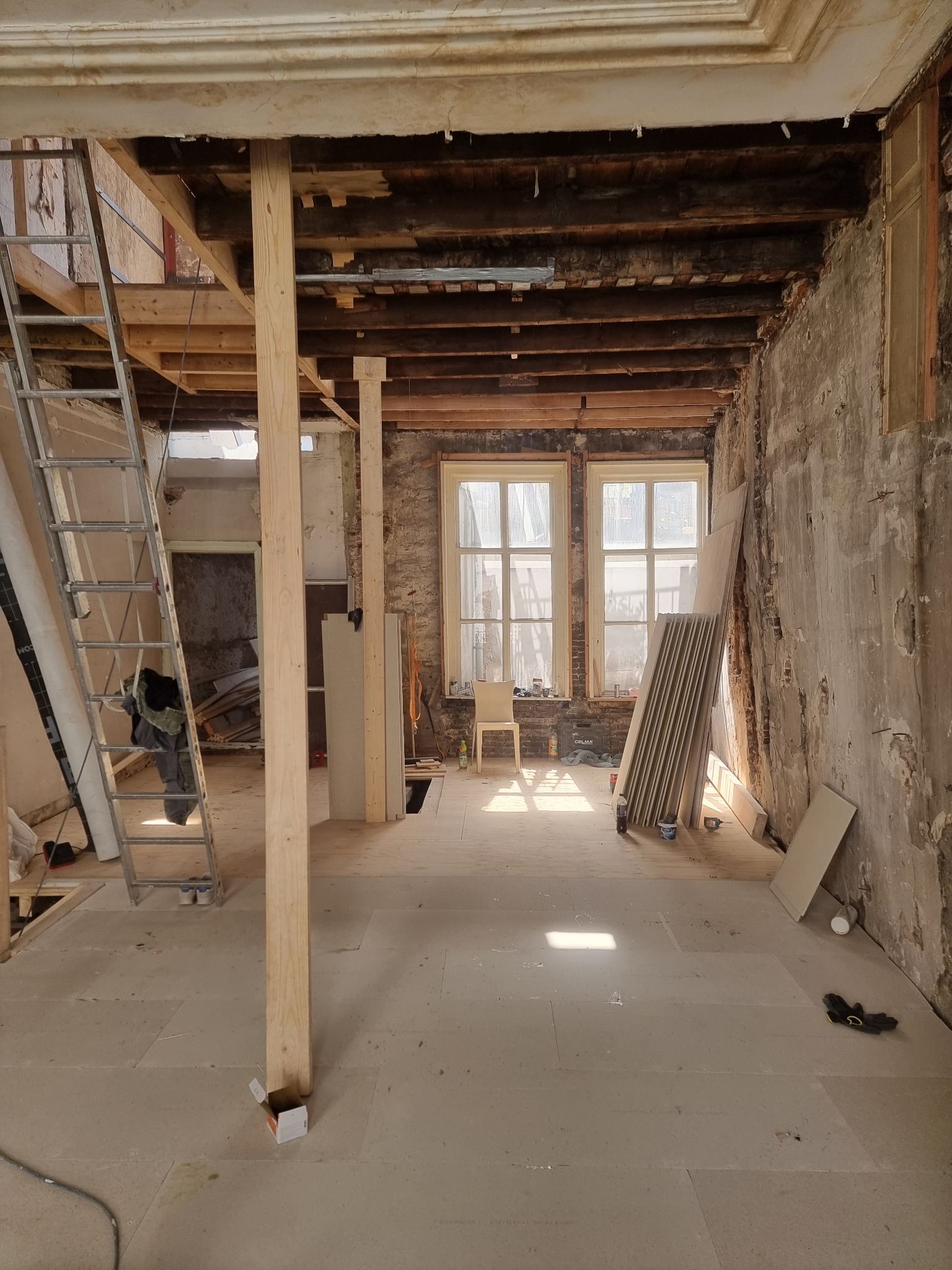 Wnętrze w trakcie kompleksowego remontu w Połczynie-Zdroju, widoczne odsłonięte drewniane belki stropowe, surowe ściany, podłoga przygotowana pod wykończenie, drabina i materiały budowlane.