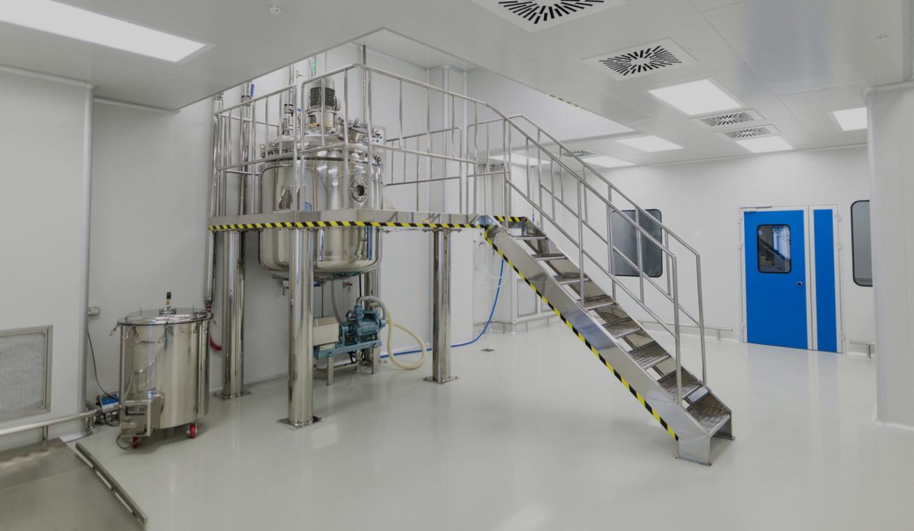 Wnętrze sterylnego pomieszczenia z dużą, metalową instalacją procesową na podeście, dostępną przez metalowe schody z żółto-czarnymi oznaczeniami ostrzegawczymi, oraz dodatkowym zbiornikiem...