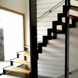 Nowoczesne schody z drewnianymi stopniami i czarną metalową konstrukcją, zabezpieczone poziomymi linkami. Widok z dołu, jasne wnętrze.