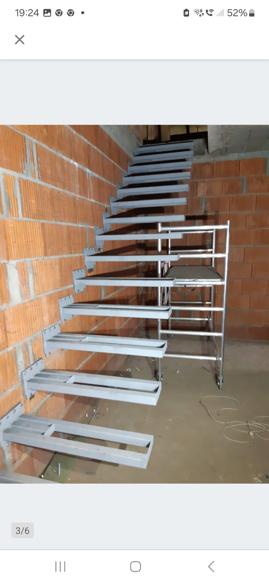 Montaż metalowych schodów wspornikowych przy ceglanej ścianie. Widoczne elementy mocujące i rusztowanie pomocnicze. Surowy stan wykończenia wnętrza.