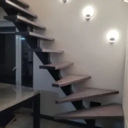 Nowoczesne schody z drewnianymi stopniami i czarną, metalową konstrukcją nośną, oświetlone trzema okrągłymi lampami na ścianie.