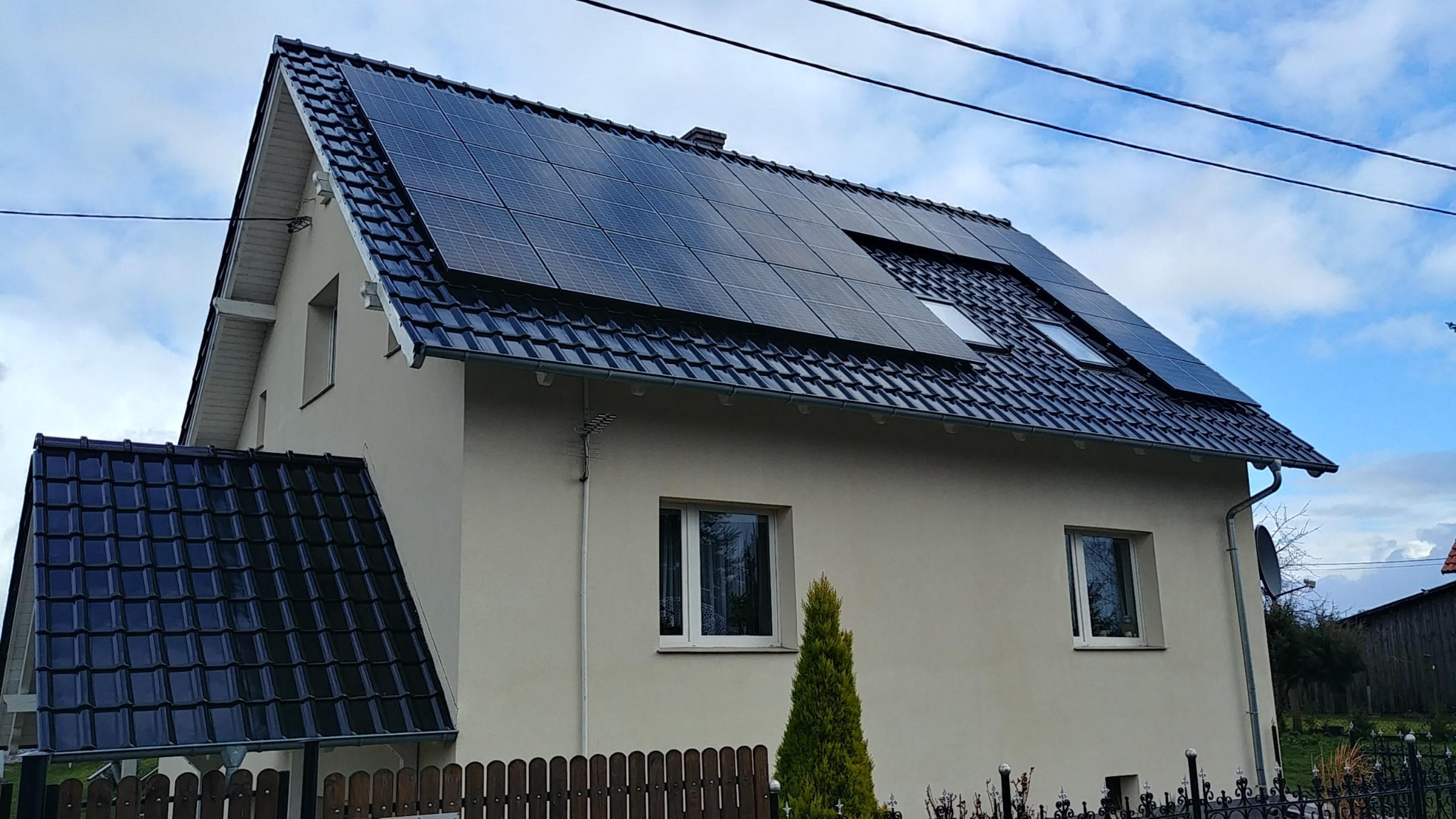 Dom jednorodzinny z panelami słonecznymi na dachu, widoczne okna dachowe i antena satelitarna.