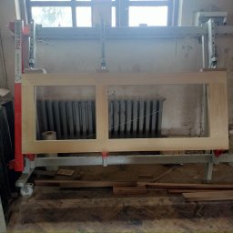 Dąbi - Surowa rama okienna z jasnego drewna zamocowana w maszynie stolarskiej CRAFTDREW PSK4000, widoczny grzejnik żeliwny w tle.