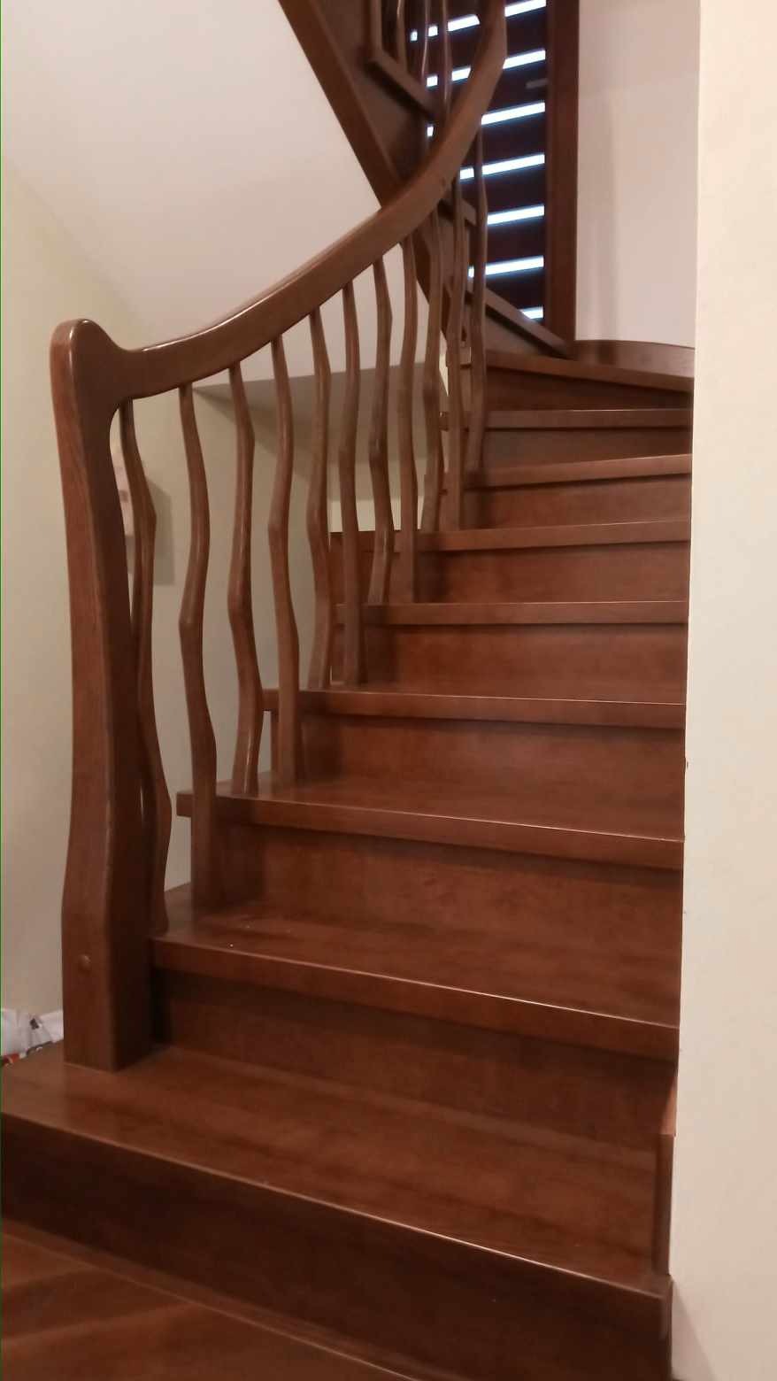 Brązowe, drewniane schody z zakrętem i ozdobną balustradą w ciepłym oświetleniu.