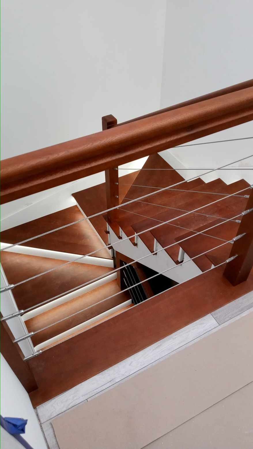 Nowoczesne schody z drewnianymi stopniami w odcieniach brązu i metalowymi linkami zabezpieczającymi, widok z góry.