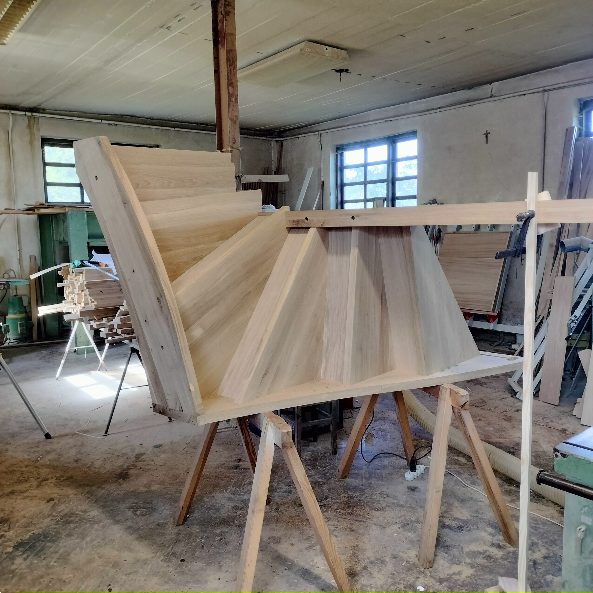 Surowe drewniane schody na kozłach w warsztacie stolarskim, widoczne okna w tle i narzędzia.