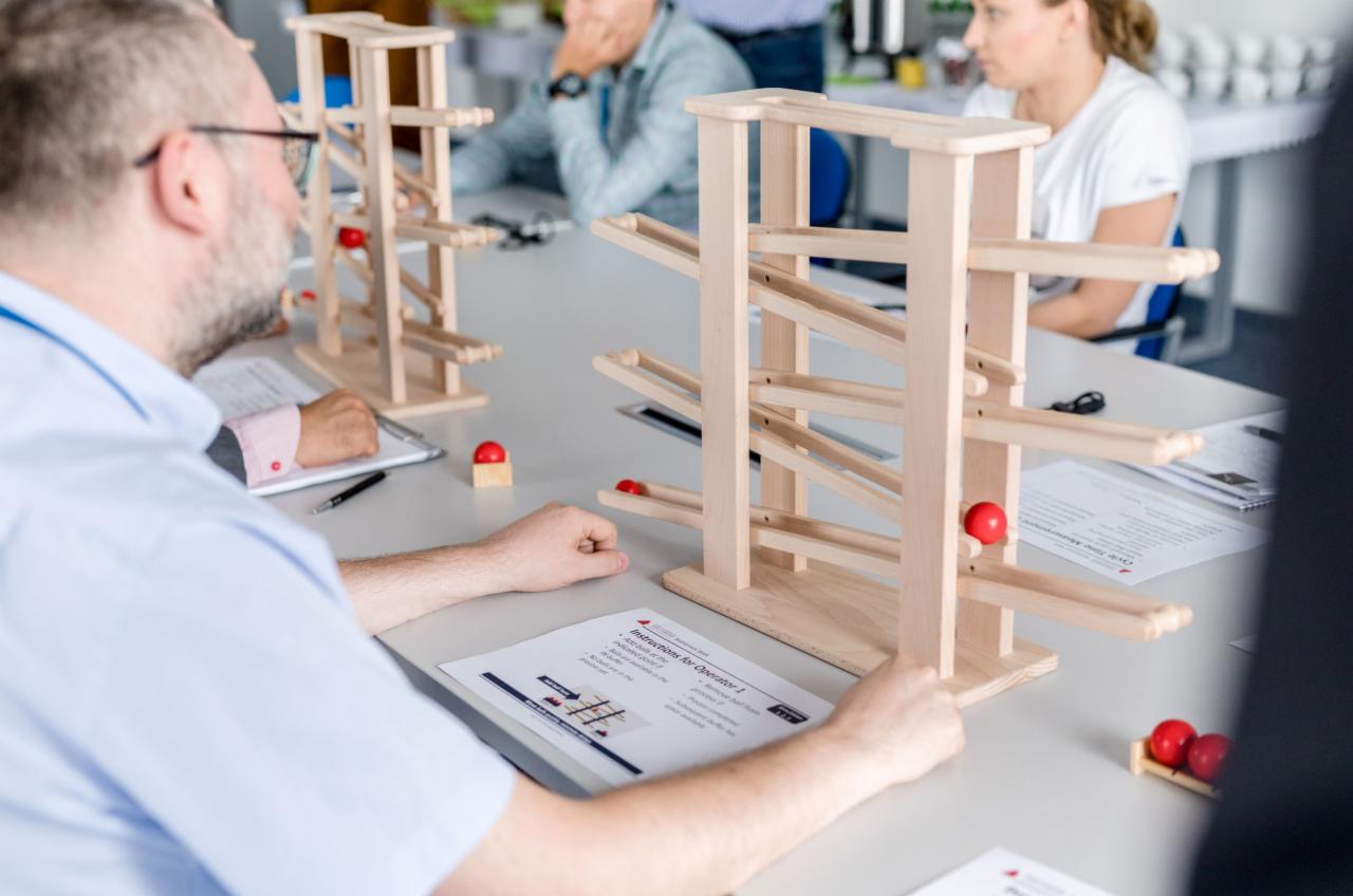 Uczestnicy szkolenia menedżerskiego pracują z drewnianymi konstrukcjami torów kulkowych, instrukcje na stole, ćwiczenie zespołowe.