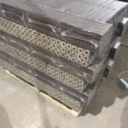 Paleta z ułożonymi kostkami opału drzewnego, owiniętymi folią, widoczne otwory w kostkach, szare tło betonowej podłogi.