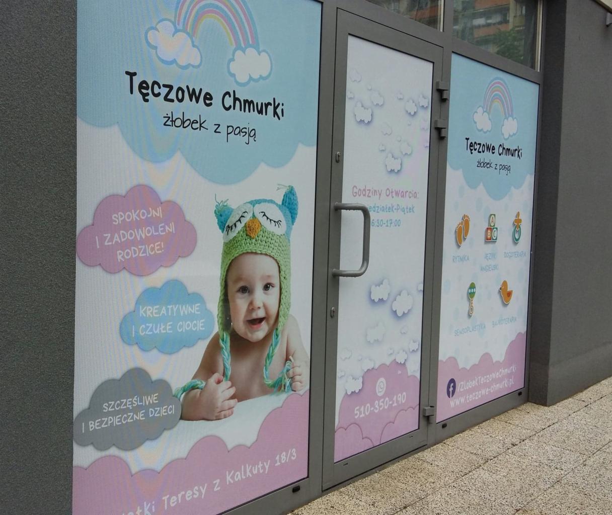 Reklama placówki opiekuńczej z uśmiechniętym niemowlęciem w zielonej czapce sowy, widoczna na drzwiach wejściowych z godzinami otwarcia i numerem telefonu.