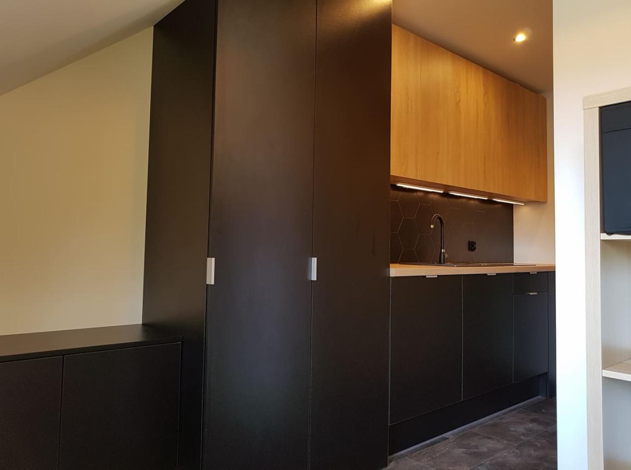 Nowoczesna łazienka z zabudową meblową w kolorze czarnym, drewnianymi szafkami wiszącymi i heksagonalnymi płytkami nad blatem.