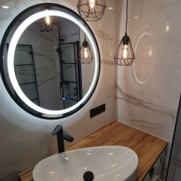 mark-bau - Nowoczesna łazienka z okrągłym lustrem z podświetleniem LED, wiszącymi lampami w metalowych kloszach, białą umywalką nablatową na drewnianym blacie i pralką w zabudowie.