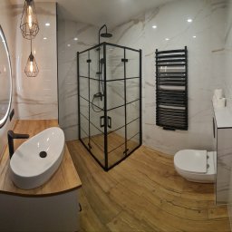 mark-bau - Nowoczesna łazienka z kabiną prysznicową w czarnej ramie, umywalką nablatową na drewnianym blacie, okrągłym lustrem z podświetleniem LED i grzejnikiem drabinkowym w kolorze czarnym.