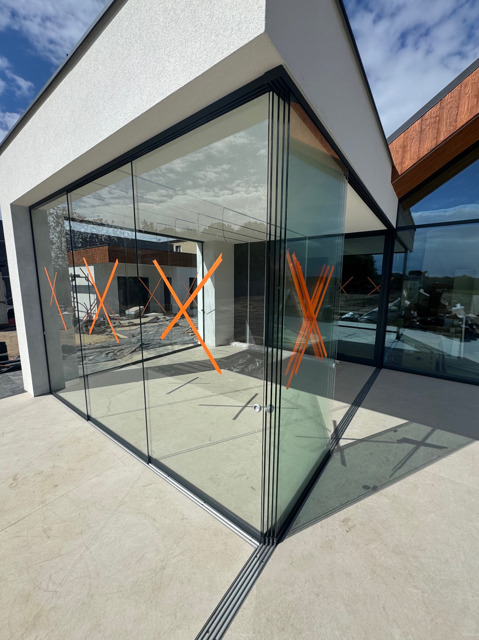 Nowoczesne, panoramiczne okna przesuwne z czarnymi ramami i pomarańczowymi oznaczeniami na szkle, widoczne z zewnątrz budynku. Minimalistyczna architektura.