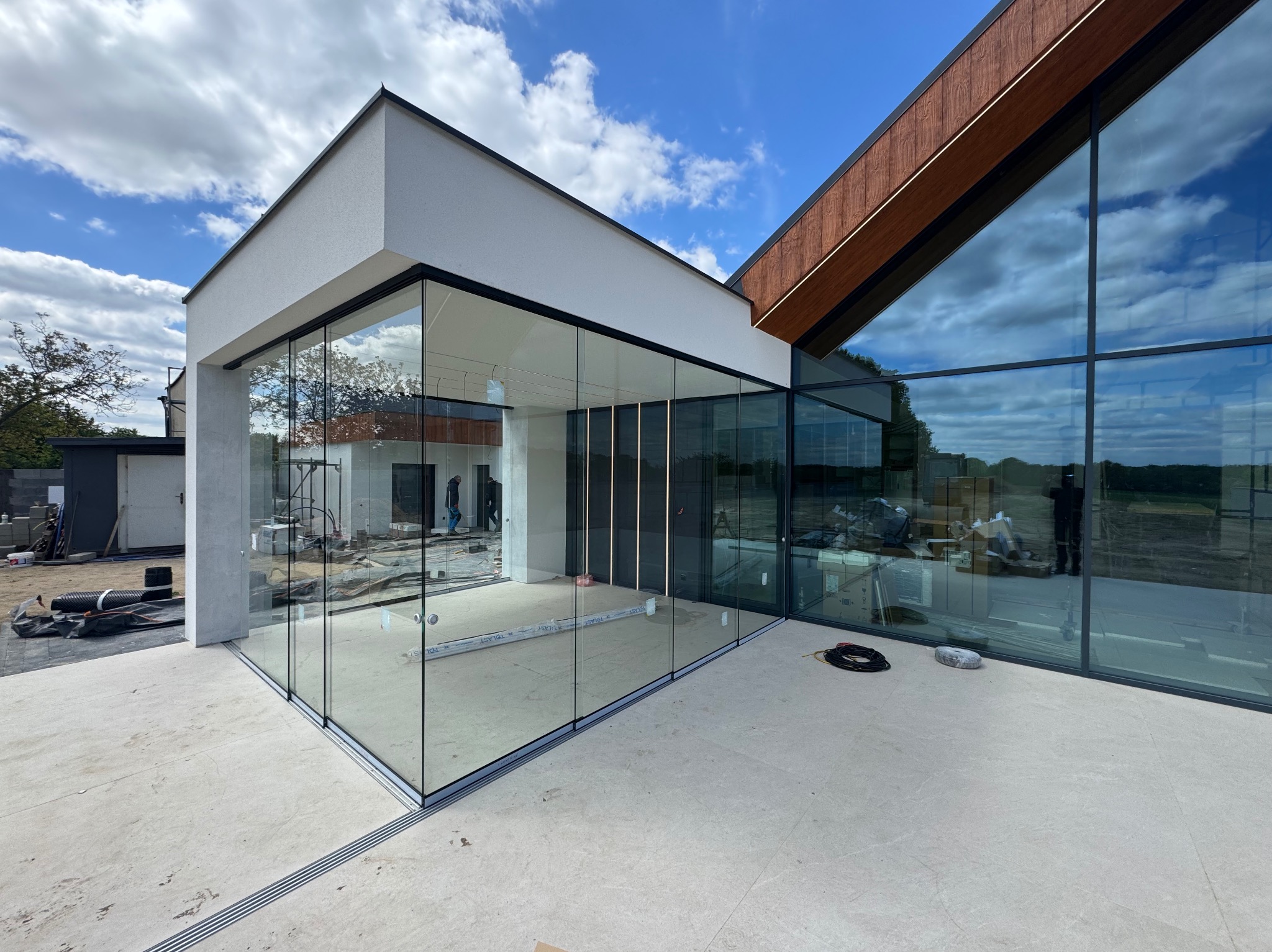 Nowoczesny dom z panoramicznymi oknami przesuwnymi, widok z zewnątrz. Minimalistyczna architektura, jasna elewacja i drewniane elementy wykończeniowe.