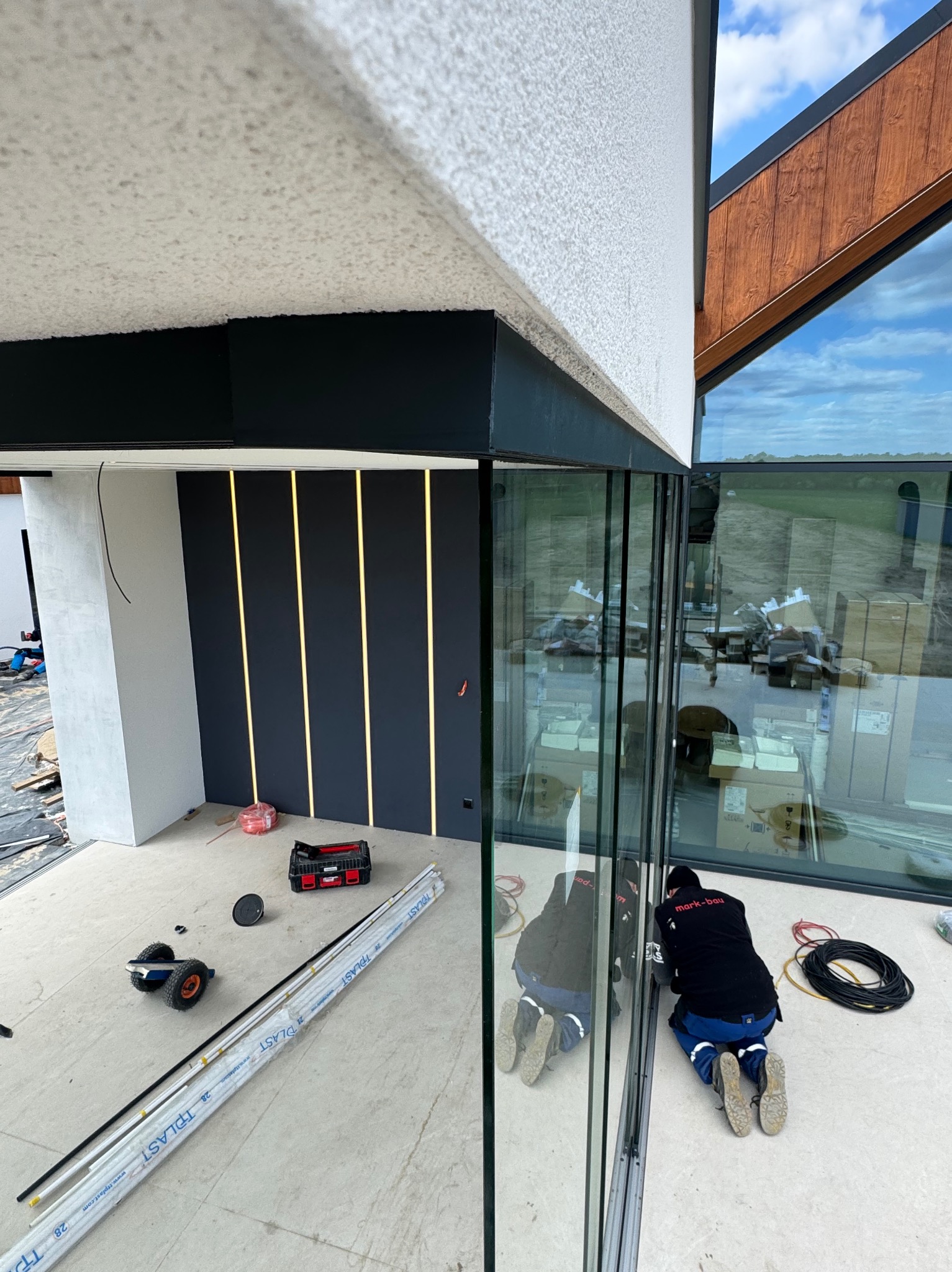 Montaż okien przesuwnych w nowoczesnym domu z oknami panoramicznymi. Widoczny pracownik w trakcie instalacji, narzędzia i profile okienne.