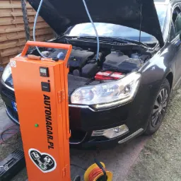 Czarny samochód z otwartą maską podczas procesu wodorowania silnika przy użyciu pomarańczowego urządzenia Autonagar.pl.