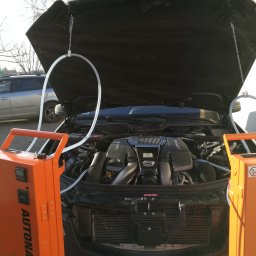 Autonagar.pl Sp.z o.o - Silnik AMG w trakcie wodorowania za pomocą pomarańczowego urządzenia Autonagar.pl, widoczne przewody i otwarty przód samochodu.