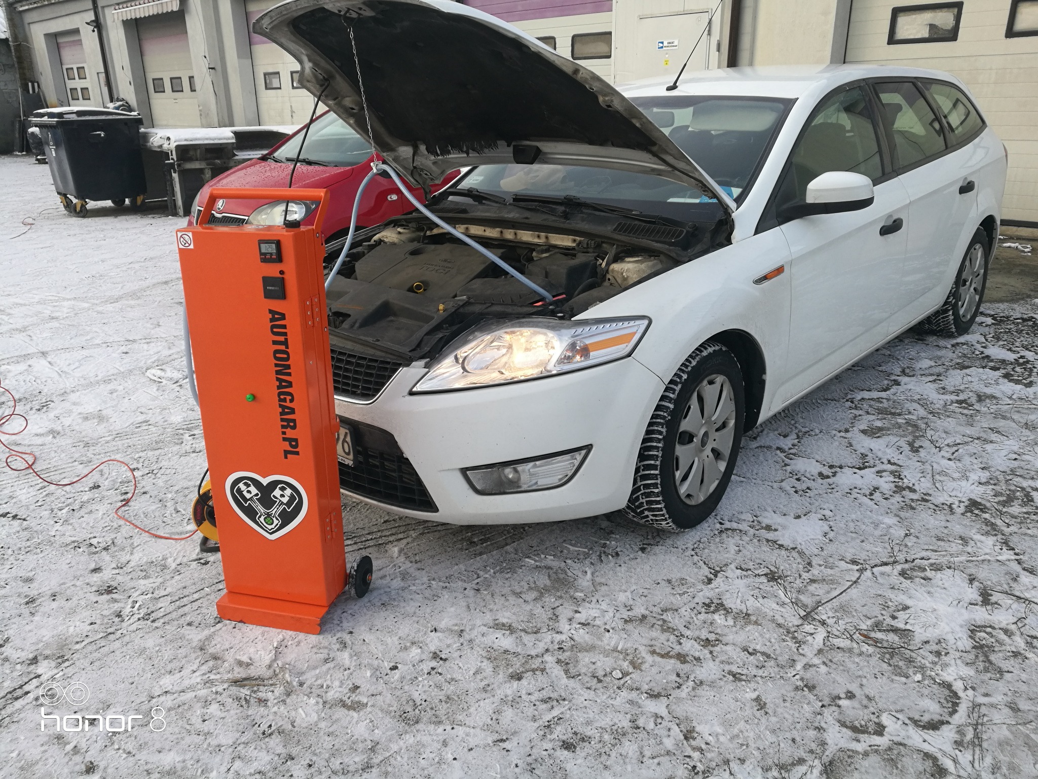 Wodorowanie silnika Forda Mondeo kombi na zewnątrz warsztatu, pomarańczowe urządzenie Autonagar.pl podłączone do silnika, śnieg na ziemi.